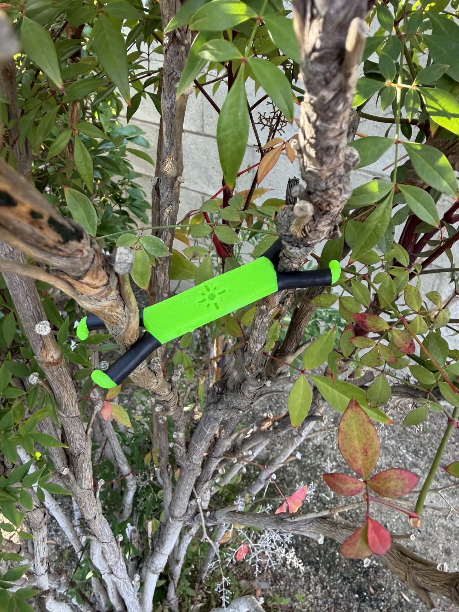 Shine Spine Branch Spreader Radiant Grove Green 2inch gardening tool attached to a tree branch with green leaves in the background.