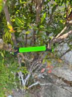 Shine Spine Branch Spreader Radiant Grove Green 3 1/2inch gardening tool attached to a tree branch with green leaves in the background.